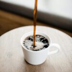 Donations Steaming black coffee being poured into a white ceramic mug on a wooden table.